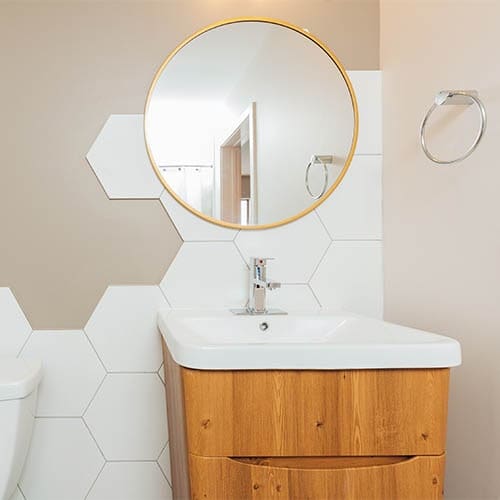 brown bathroom vanity with white sink and gold circular mirror