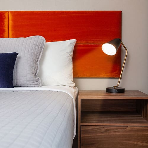 wood bedside table with gold lamp shining on bed